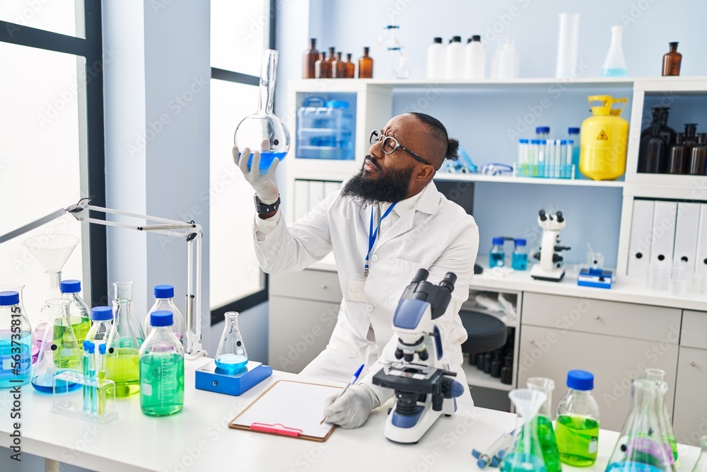 Young african american man wearing scientist uniform holding test tube at laboratory Young african american man wearing scientist uniform holding test tube at laboratory