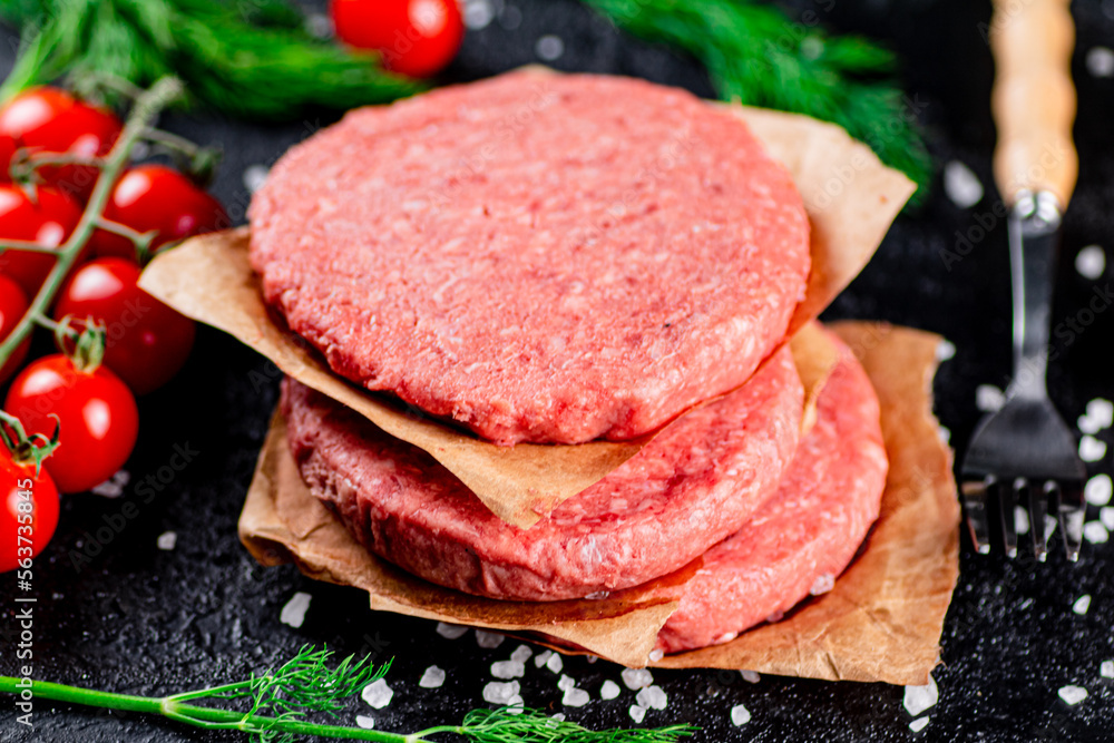 Raw burger on a table with greens and salt. 