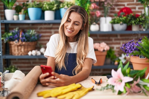Young blonde woman florist smiling confident using smartphone at florist