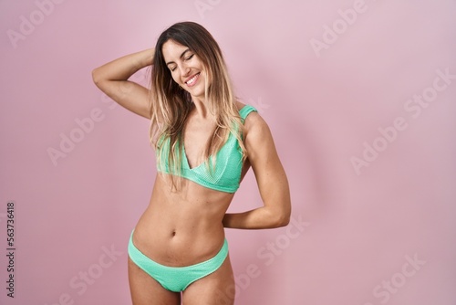 Young hispanic woman wearing bikini over pink background stretching back, tired and relaxed, sleepy and yawning for early morning