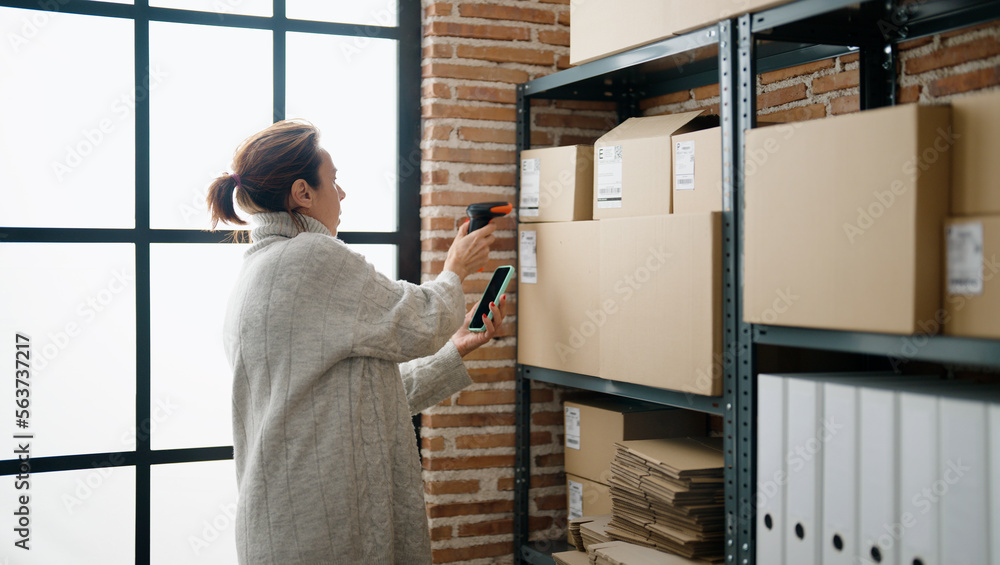 Middle age hispanic woman ecommerce business worker scanning package using barcode reader at storehouse office