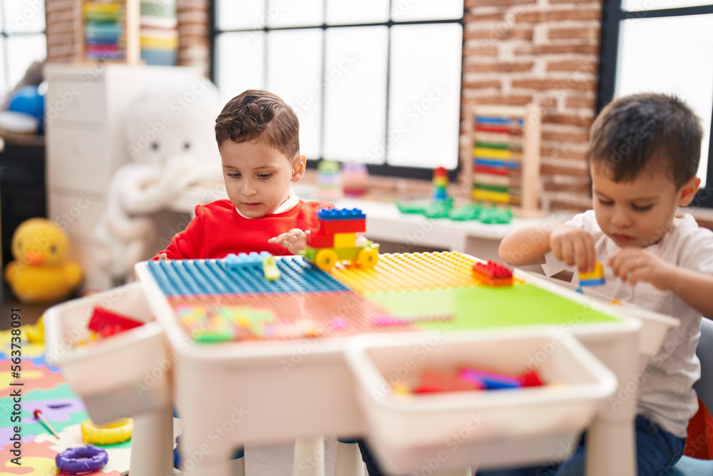 Fototapeta premium Two kids playing with construction blocks sitting on table at kindergarten