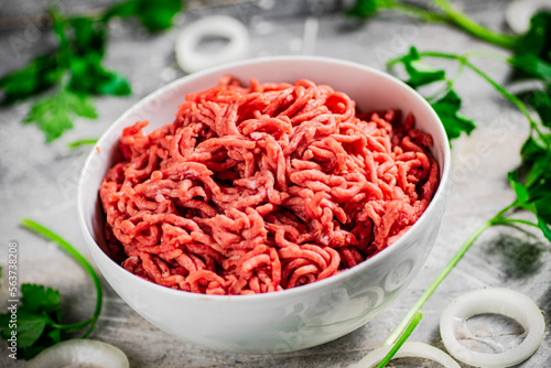 Minced meat in a bowl on a table with parsley and onion rings. 