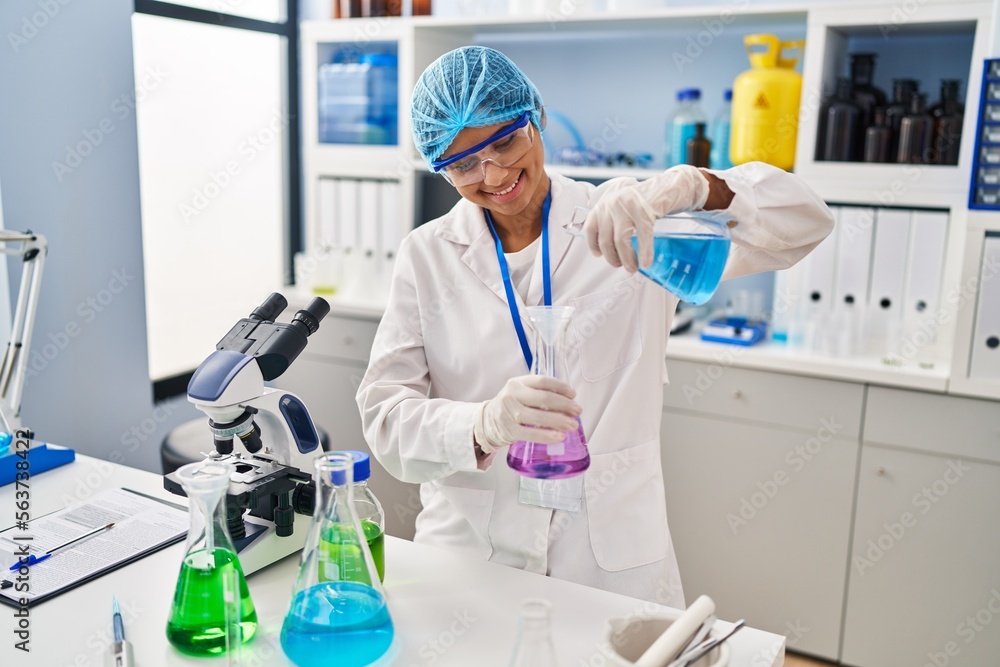 Young latin woman wearing scientist uniform measuring liquid at laboratory