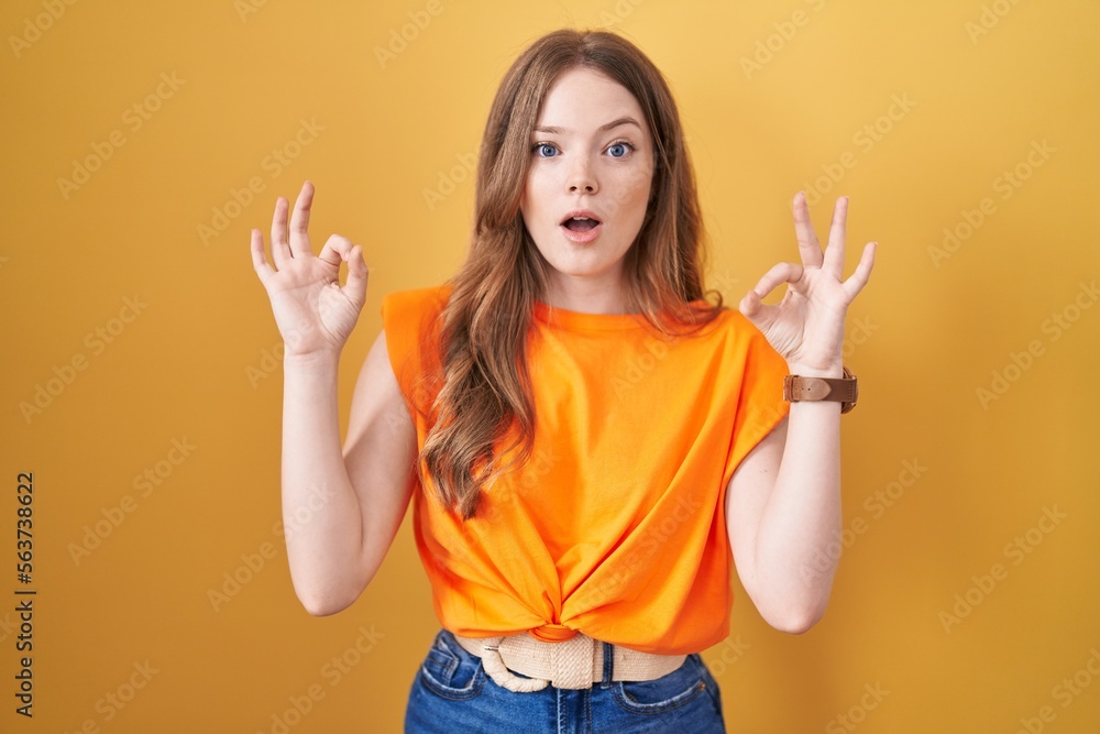 Caucasian woman standing over yellow background looking surprised and shocked doing ok approval symbol with fingers. crazy expression Caucasian woman standing over yellow background looking surprised and shocked doing ok approval symbol with fingers. crazy expression