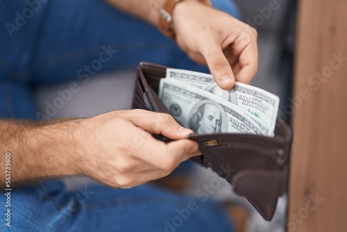 Young caucasian man holding dollars on wallet sitting on sofa at street