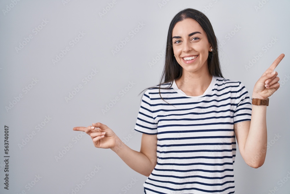 Young brunette woman wearing striped t shirt smiling confident pointing with fingers to different directions. copy space for advertisement Young brunette woman wearing striped t shirt smiling confident pointing with fingers to different directions. copy space for advertisement