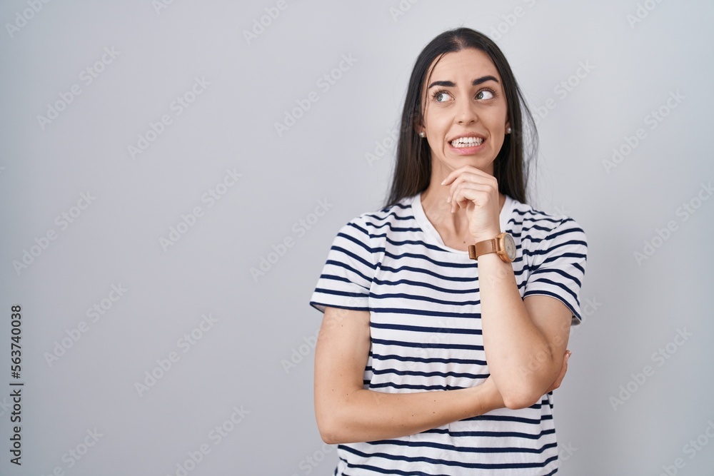 Young brunette woman wearing striped t shirt thinking worried about a question, concerned and nervous with hand on chin Young brunette woman wearing striped t shirt thinking worried about a question, concerned and nervous with hand on chin