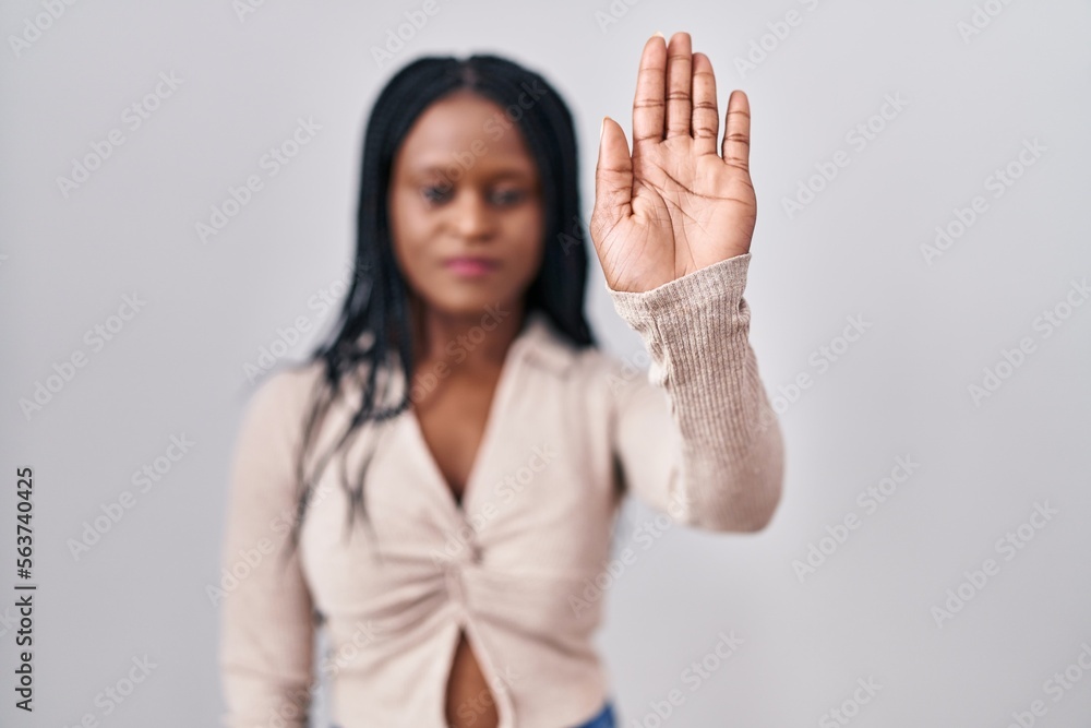 African woman with braids standing over white background doing stop sing with palm of the hand. warning expression with negative and serious gesture on the face.