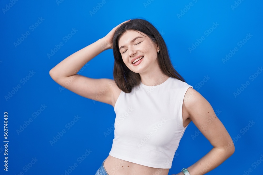 Young caucasian woman standing over blue background smiling confident touching hair with hand up gesture, posing attractive and fashionable Young caucasian woman standing over blue background smiling confident touching hair with hand up gesture, posing attractive and fashionable