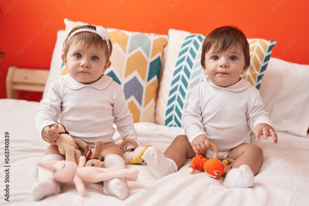 Two adorable babies holding toy sitting on bed at bedroom Two adorable babies holding toy sitting on bed at bedroom