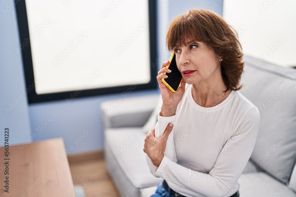 Middle age woman talking on smartphone with worried expression at home Middle age woman talking on smartphone with worried expression at home