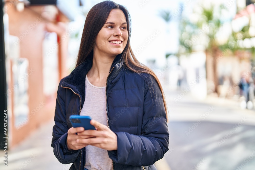 Fototapeta premium Young beautiful hispanic woman smiling confident using smartphone at street
