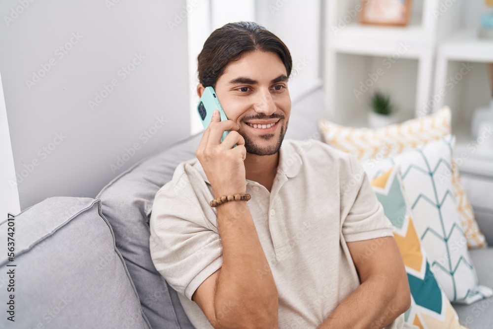 Young hispanic man talking on the smartphone sitting on sofa at home Young hispanic man talking on the smartphone sitting on sofa at home