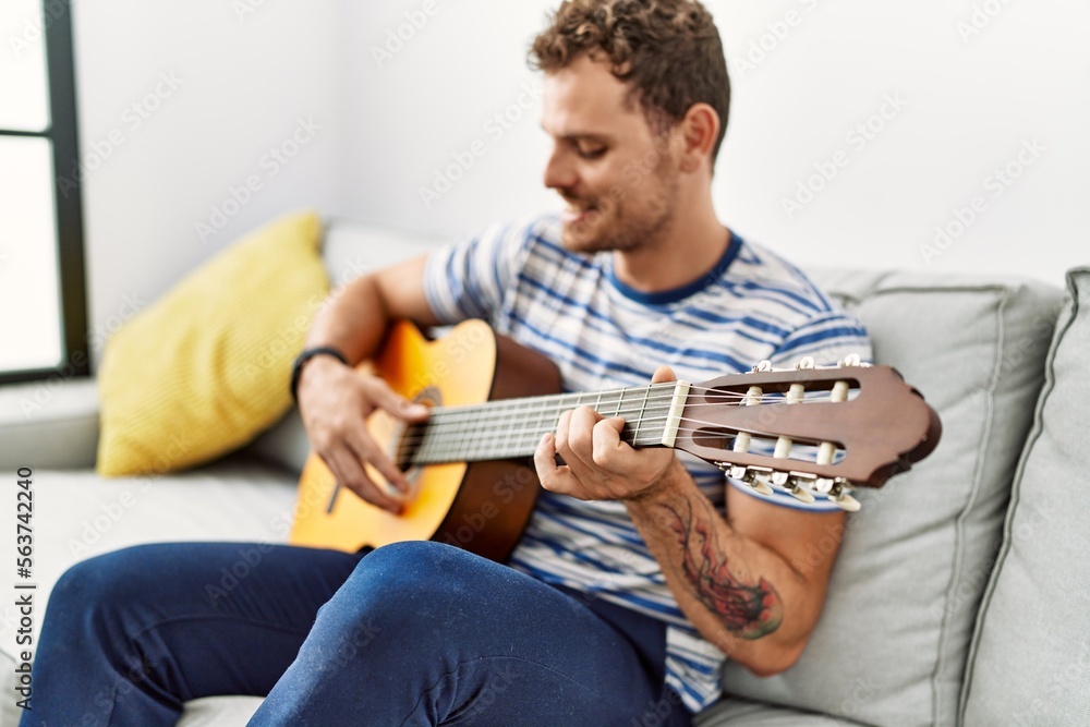 Young hispanic man smiling confident playing classical guitar at home