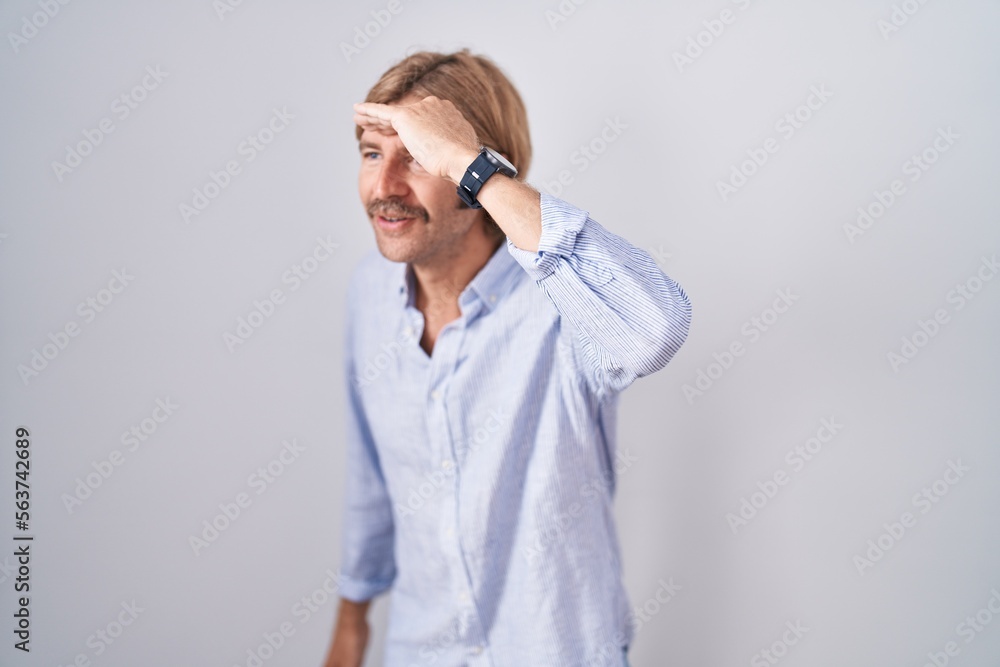 Caucasian man with mustache standing over white background very happy and smiling looking far away with hand over head. searching concept. Caucasian man with mustache standing over white background very happy and smiling looking far away with hand over head. searching concept.