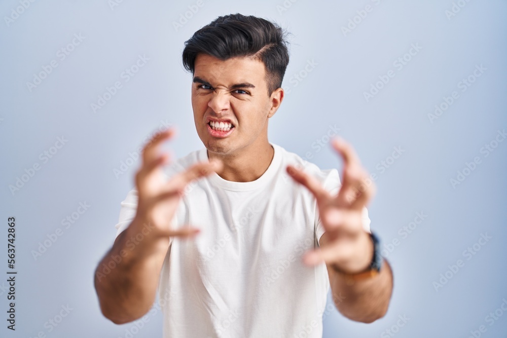 Hispanic man standing over blue background shouting frustrated with rage, hands trying to strangle, yelling mad Hispanic man standing over blue background shouting frustrated with rage, hands trying to strangle, yelling mad