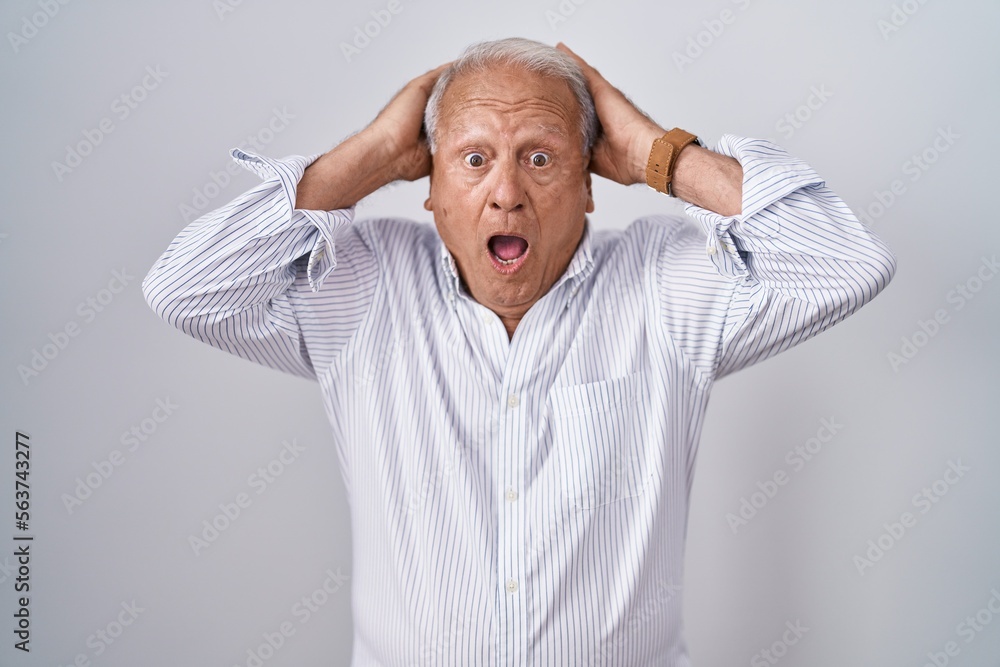 Senior man with grey hair standing over isolated background crazy and scared with hands on head, afraid and surprised of shock with open mouth Senior man with grey hair standing over isolated background crazy and scared with hands on head, afraid and surprised of shock with open mouth