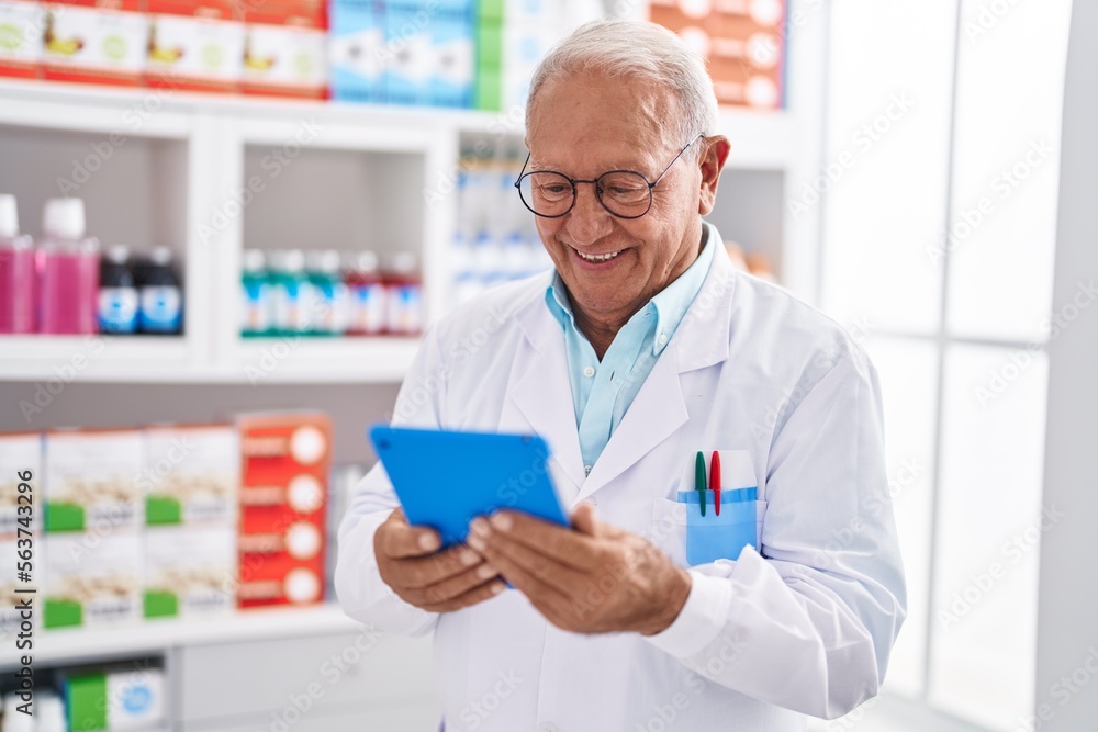 Senior grey-haired man pharmacist using touchpad at pharmacy