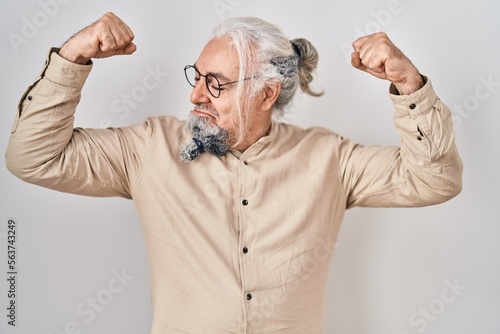Middle age man with grey hair standing over isolated background showing arms muscles smiling proud. fitness concept. © Krakenimages.com