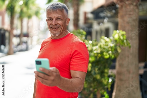 Middle age grey-haired man smiling confident using smartphone at street