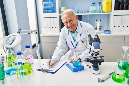 Senior man wearing scientist uniform measuring liquid at laboratory