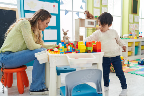 Teacher and toddler playing with construction blocks sitting on table at kindergarten