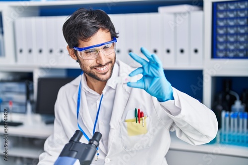 Young hispanic man scientist smiling confident holding sample at laboratory