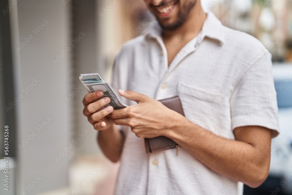 Fototapeta premium Young arab man smiling confident counting dollars at street
