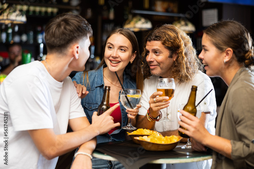 Group of happy carefree people spending time in pub, drinking beer with snacks and chatting in friendly way
