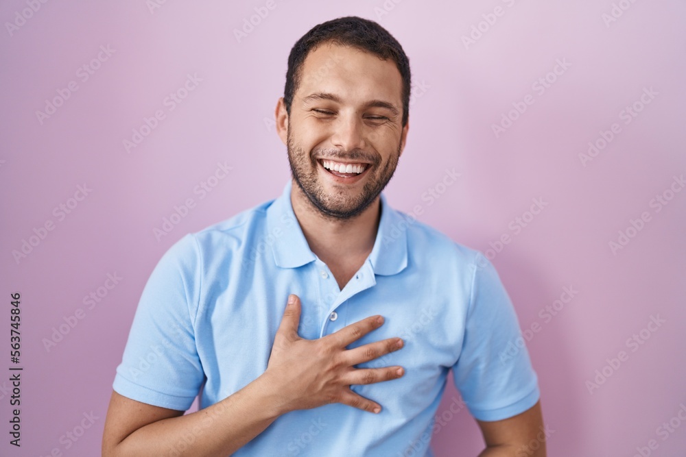 Hispanic man standing over pink background smiling and laughing hard out loud because funny crazy joke with hands on body. Hispanic man standing over pink background smiling and laughing hard out loud because funny crazy joke with hands on body.