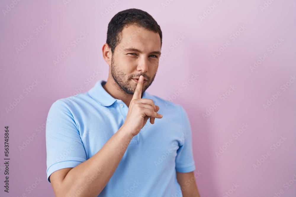 Hispanic man standing over pink background asking to be quiet with finger on lips. silence and secret concept.