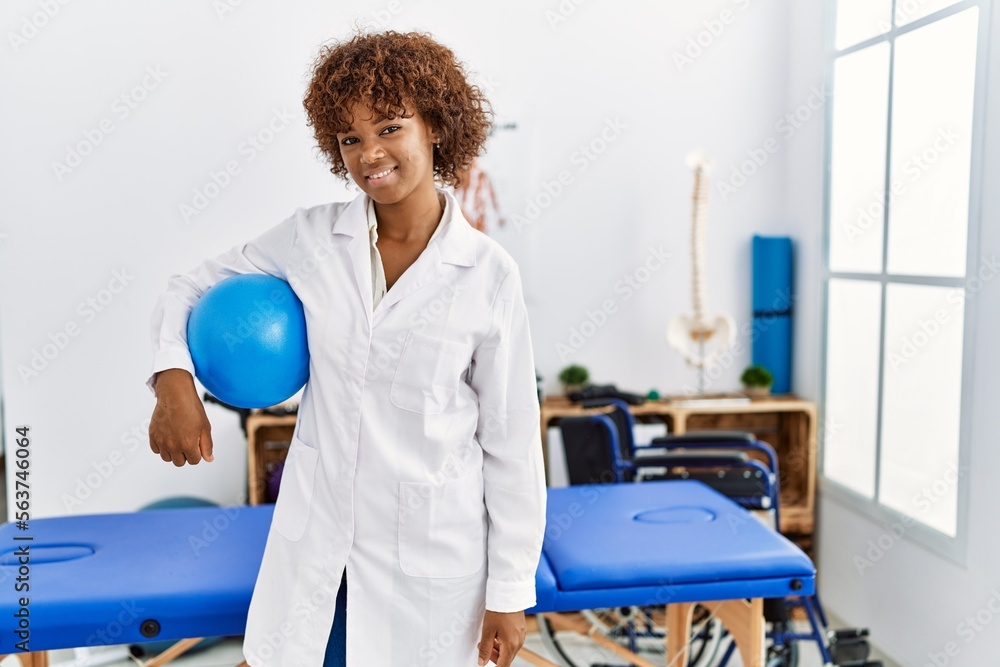 Young african american woman wearing physio uniform holding fit ball at clinic Young african american woman wearing physio uniform holding fit ball at clinic