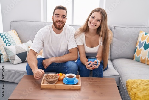 Man and woman couple having breakfast sitting on sofa at home
