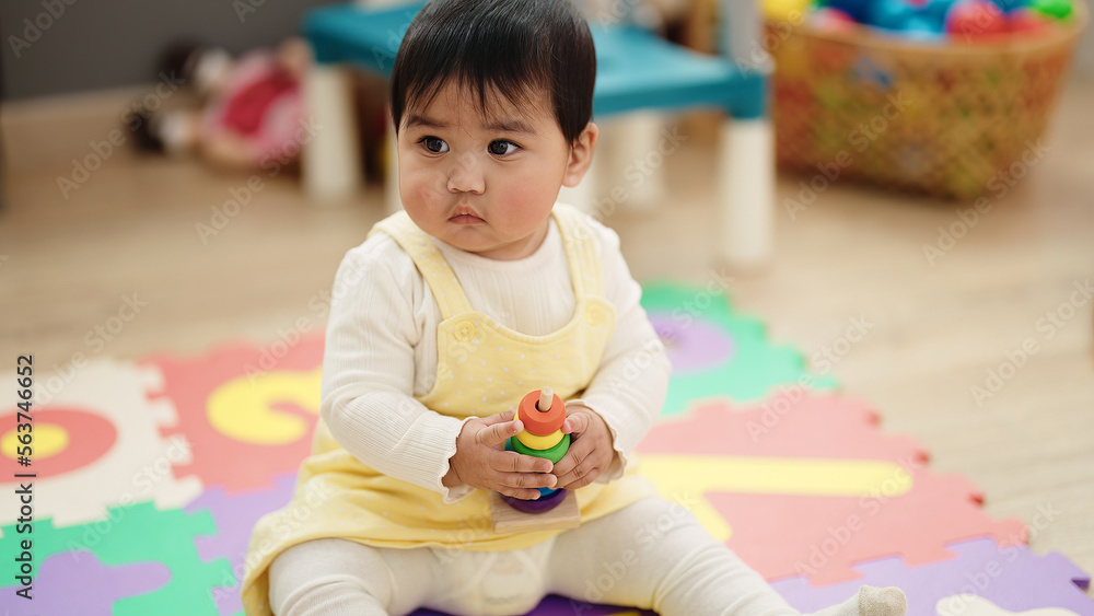 Adorable hispanic baby playing with hoops sitting on floor at kindergarten Adorable hispanic baby playing with hoops sitting on floor at kindergarten