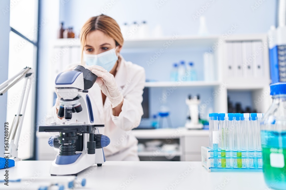 Young blonde woman scientist wearing medical mask using microscope at laboratory Young blonde woman scientist wearing medical mask using microscope at laboratory