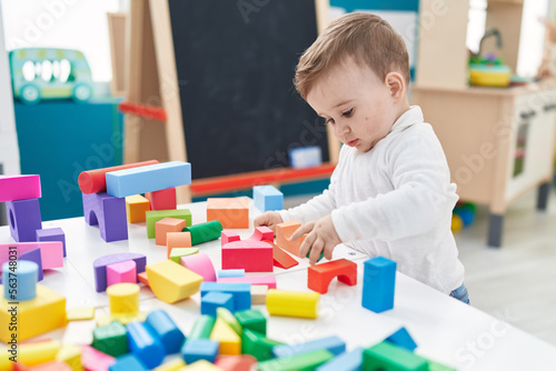 Adorable caucasian baby playing with construction blocks standing at kindergarten