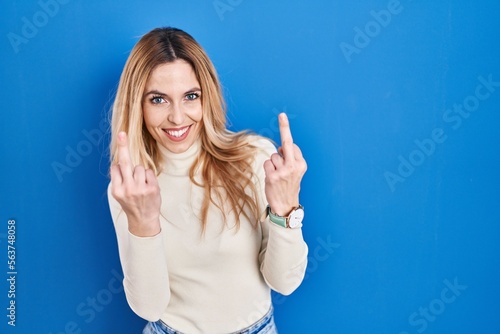 Young caucasian woman standing over blue background showing middle finger doing fuck you bad expression, provocation and rude attitude. screaming excited
