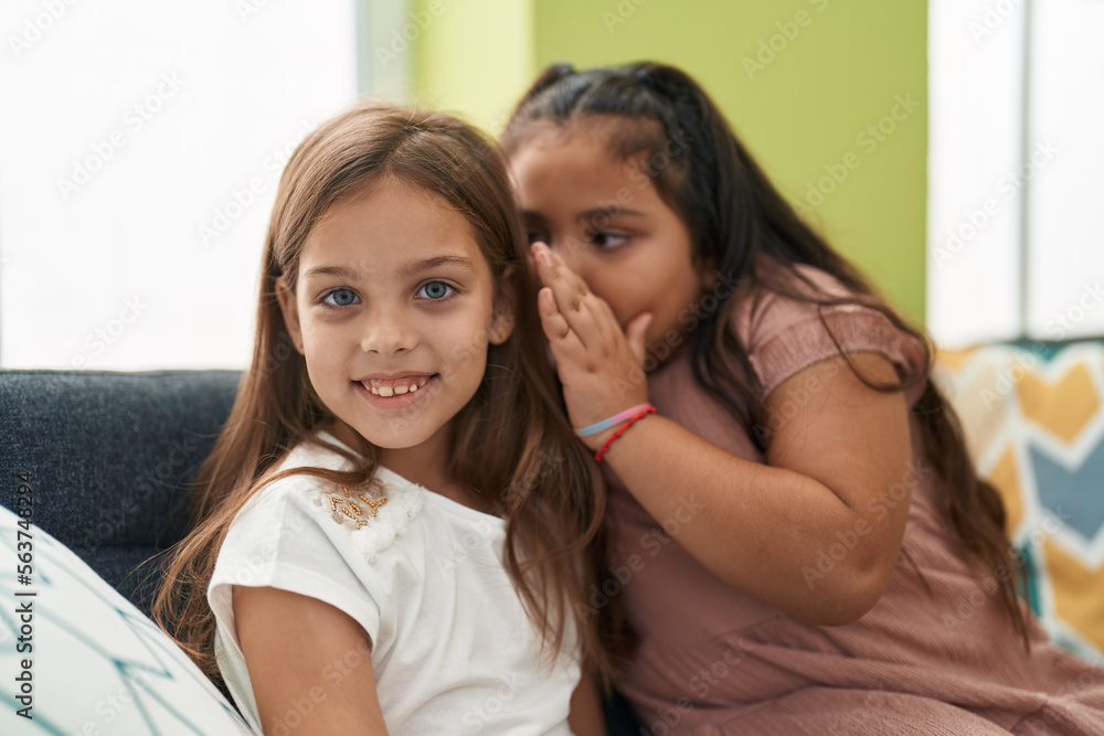 Two kids telling secret sitting on sofa at home Two kids telling secret sitting on sofa at home