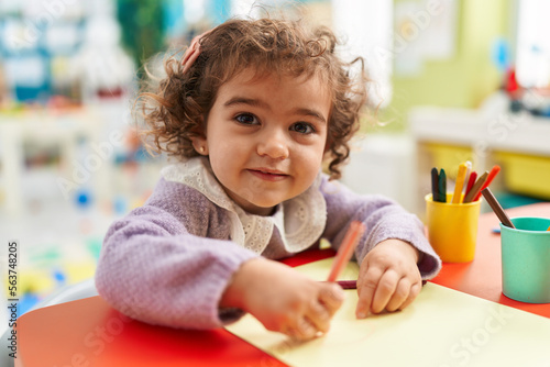 Adorable hispanic girl preschool student sitting on table drawing on paper at kindergarten