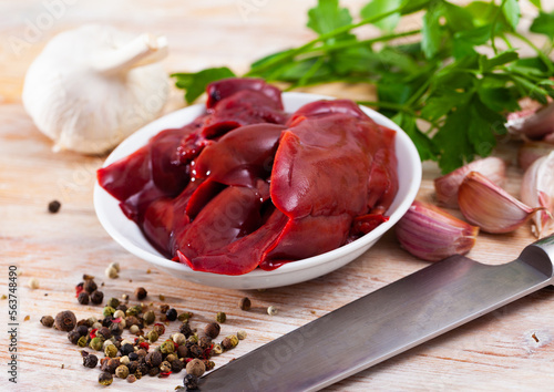 Raw rabbit liver served on wooden table with herbs, onion and garlic