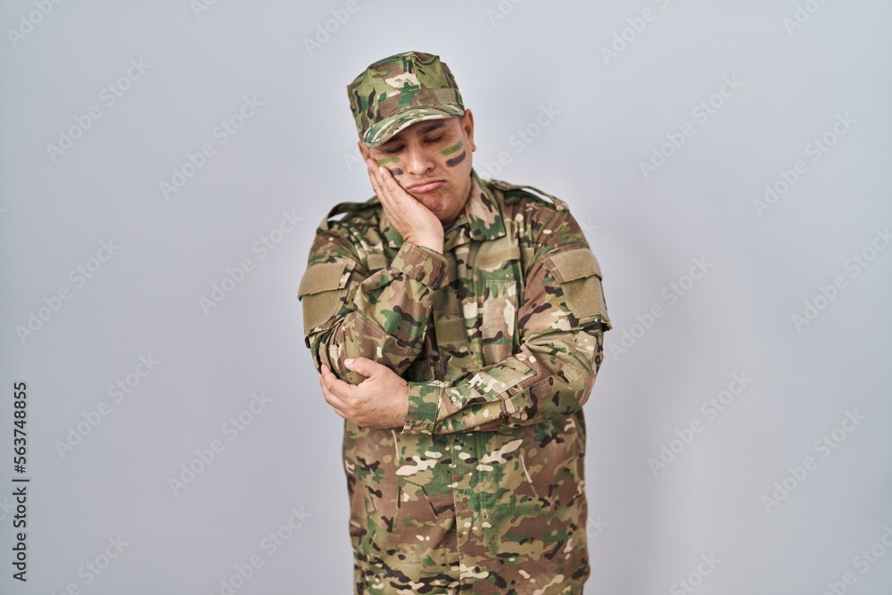 Hispanic young man wearing camouflage army uniform thinking looking tired and bored with depression problems with crossed arms. Hispanic young man wearing camouflage army uniform thinking looking tired and bored with depression problems with crossed arms.