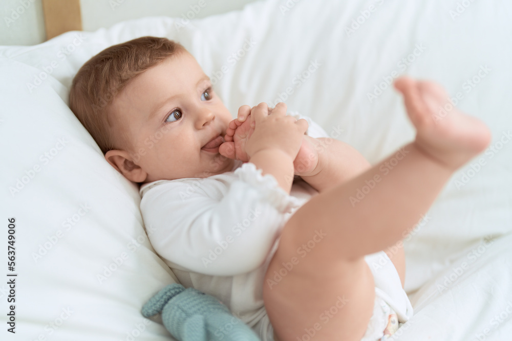 Adorable toddler lying on bed sucking feet at bedroom Adorable toddler lying on bed sucking feet at bedroom