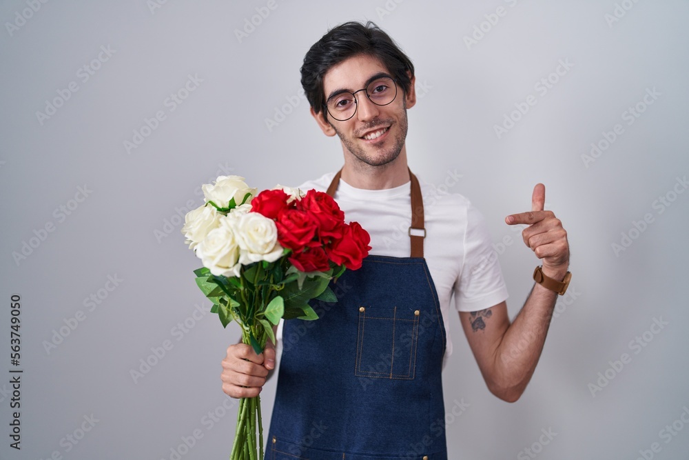 Young hispanic man holding bouquet of white and red roses looking confident with smile on face, pointing oneself with fingers proud and happy. Young hispanic man holding bouquet of white and red roses looking confident with smile on face, pointing oneself with fingers proud and happy.