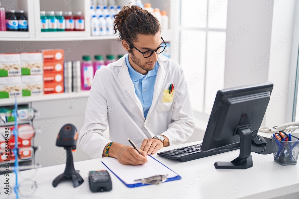 Young hispanic man pharmacist writing on document at pharmacy Young hispanic man pharmacist writing on document at pharmacy