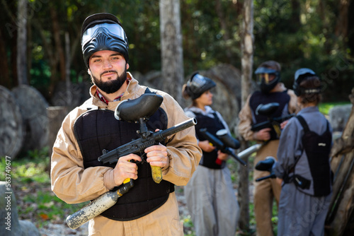 Man and his paintball sport team in protective uniform at paintball shooting range