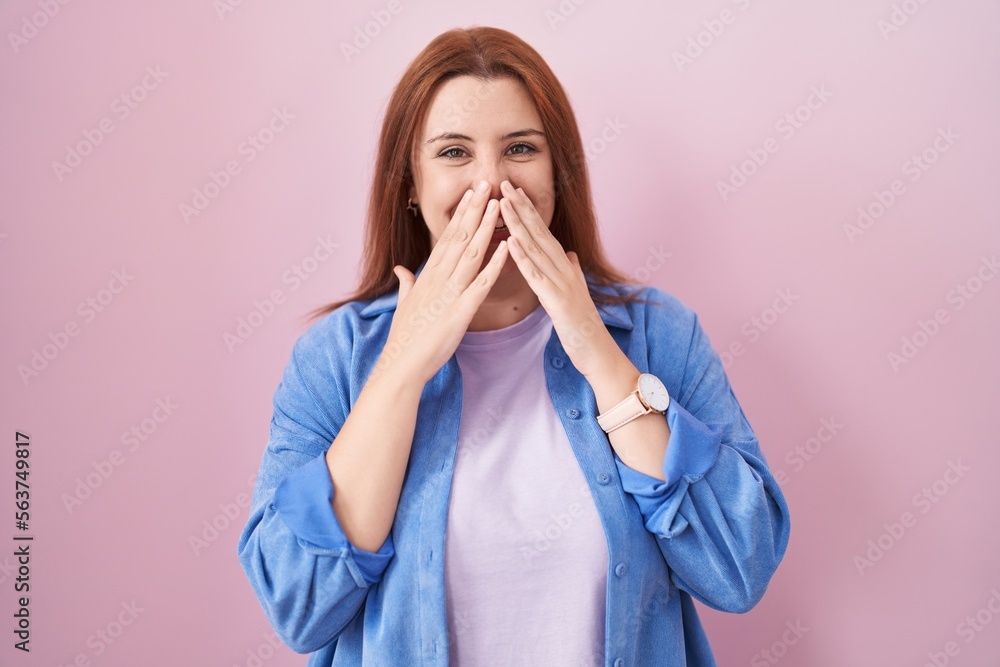 Young hispanic woman with red hair standing over pink background laughing and embarrassed giggle covering mouth with hands, gossip and scandal concept Young hispanic woman with red hair standing over pink background laughing and embarrassed giggle covering mouth with hands, gossip and scandal concept
