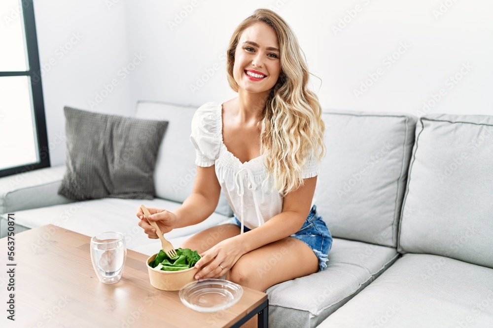 Young woman eating salad sitting on sofa at home Young woman eating salad sitting on sofa at home