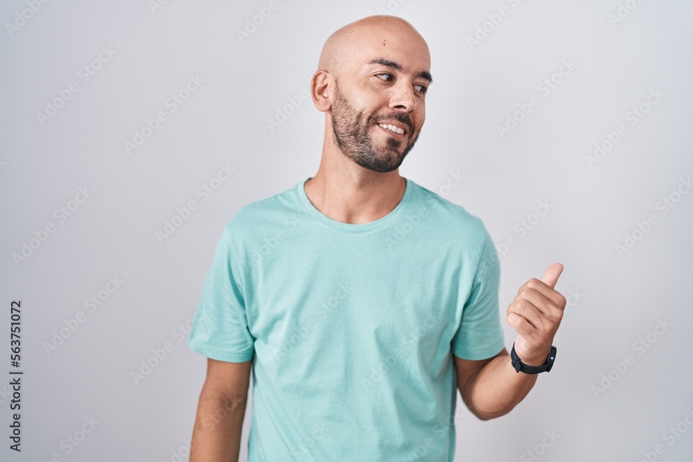 Middle age bald man standing over white background smiling with happy face looking and pointing to the side with thumb up. Middle age bald man standing over white background smiling with happy face looking and pointing to the side with thumb up.