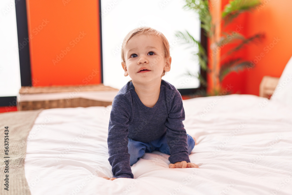 Adorable blond toddler sitting on bed with with relaxed expression at bedroom Adorable blond toddler sitting on bed with with relaxed expression at bedroom